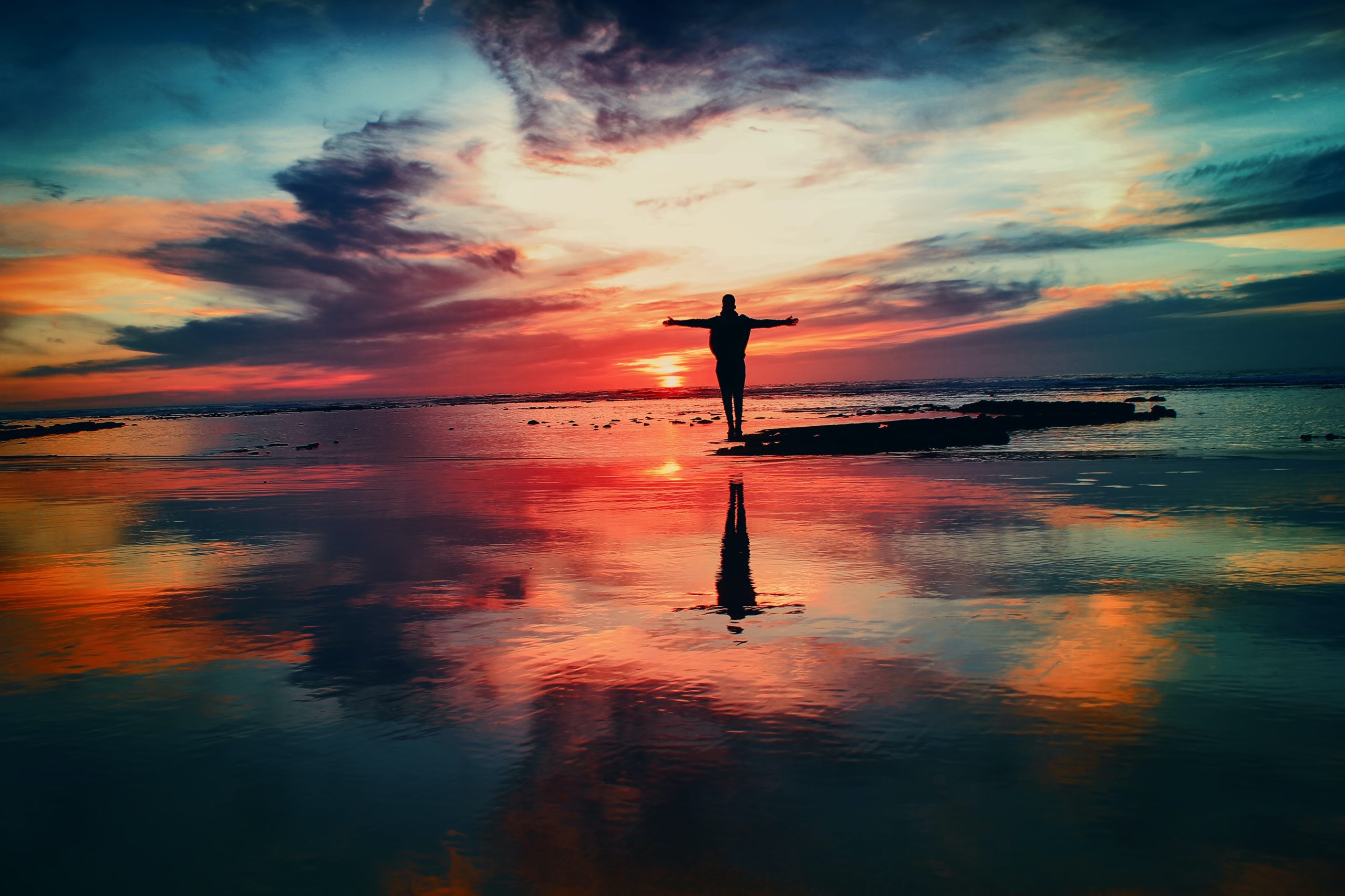 A beautiful sunrise over the still water, with person with their arms stretched out to hug the sun.