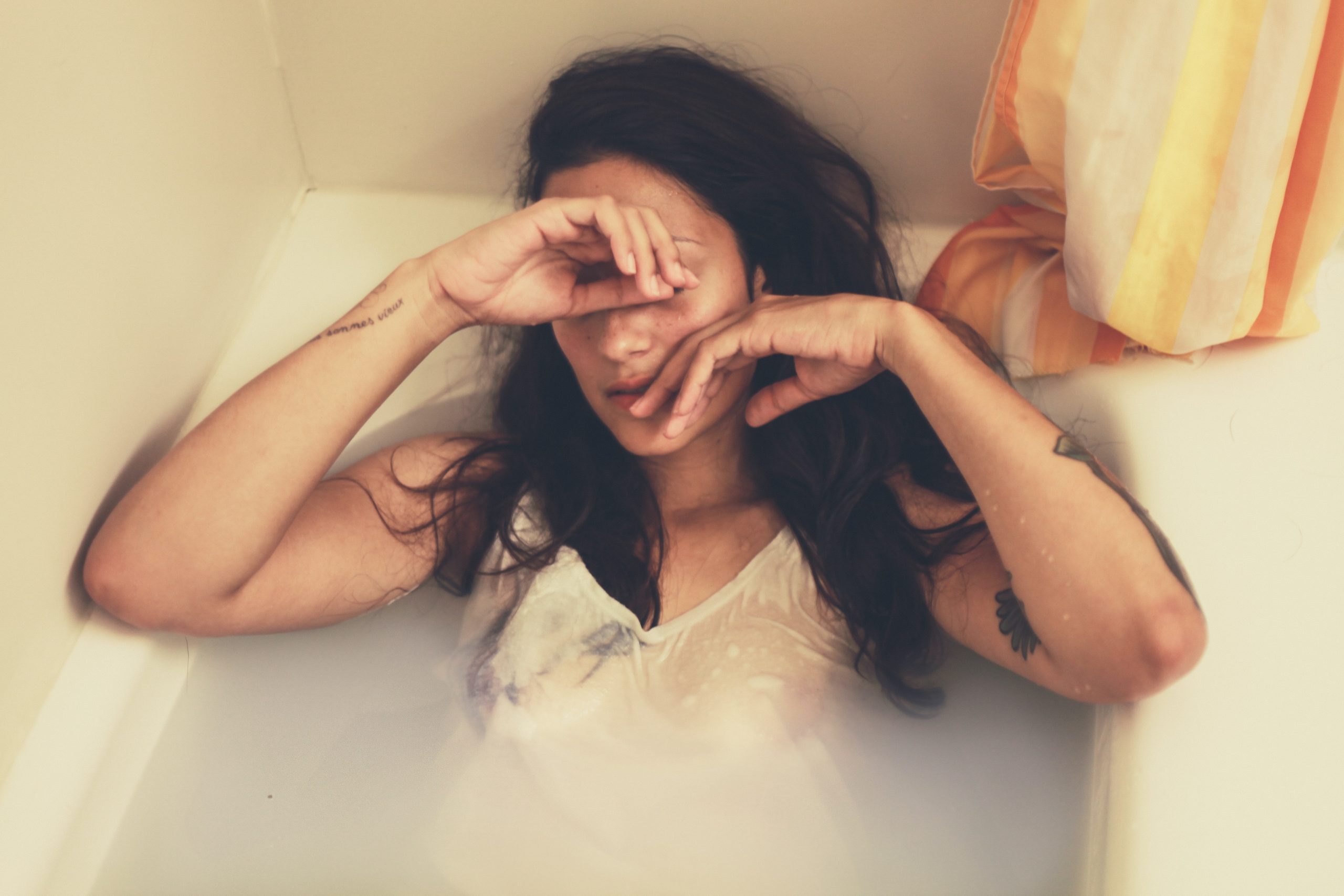 A women in a bathtub with hands to her face looking distressed